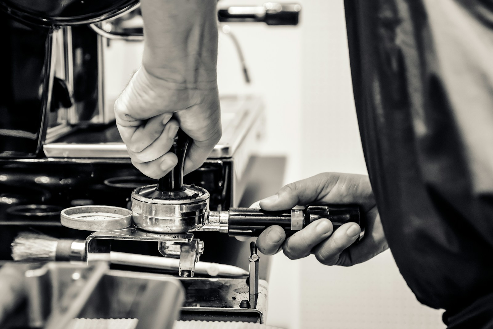 Espresso-Zubehör im Einsatz: Barista tampt Kaffeepulver im Siebträger an einer Kaffeebar