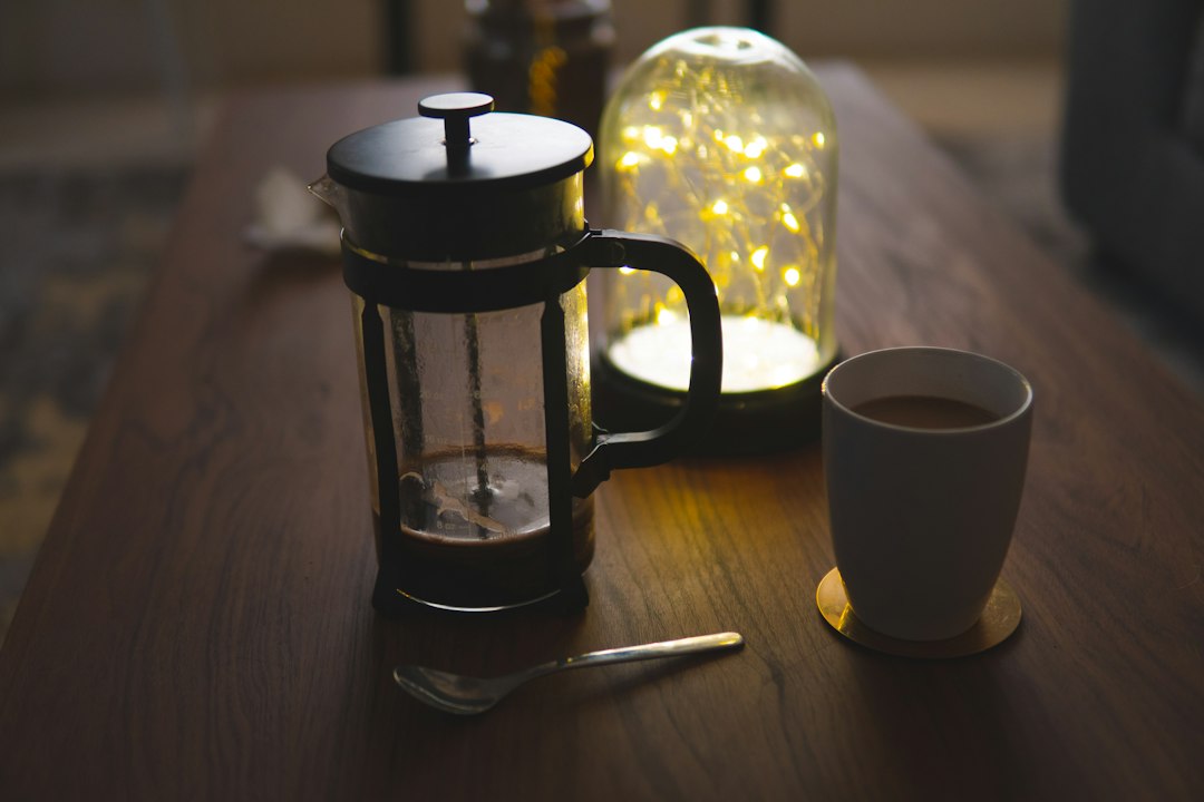French Press mit Kaffee neben einer weißen Tasse auf einem Holztisch