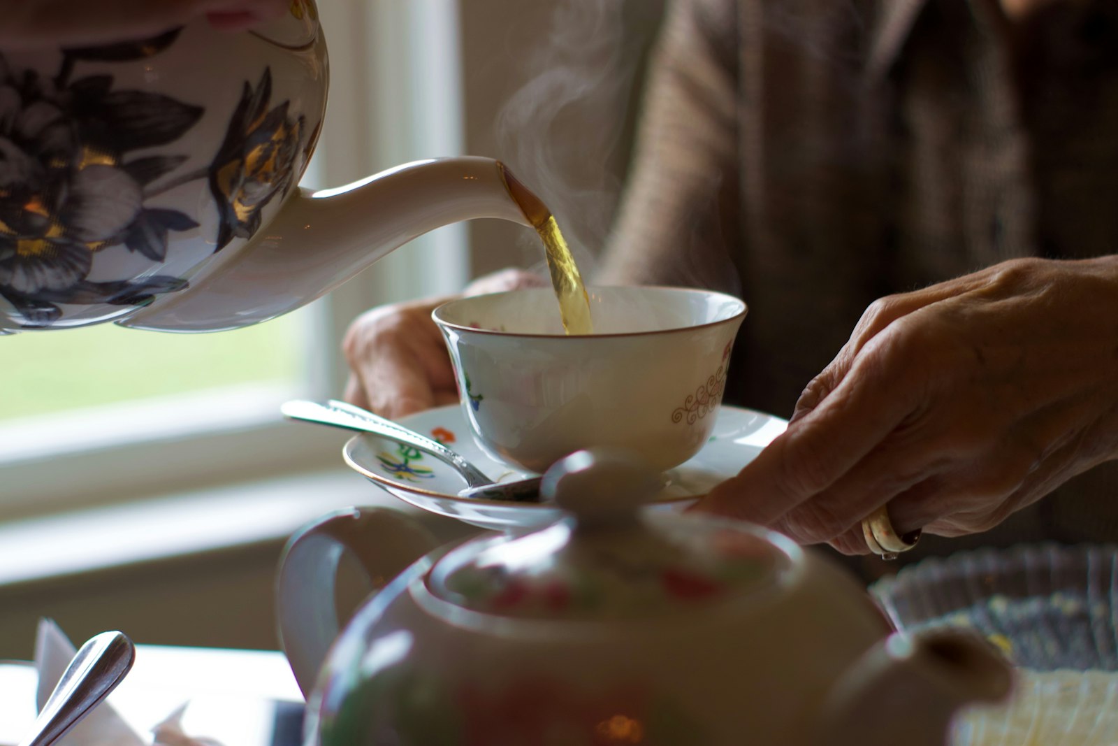 Tee aufgießen: Aus einer weißen Keramikkanne wird Tee in eine Tasse gegossen