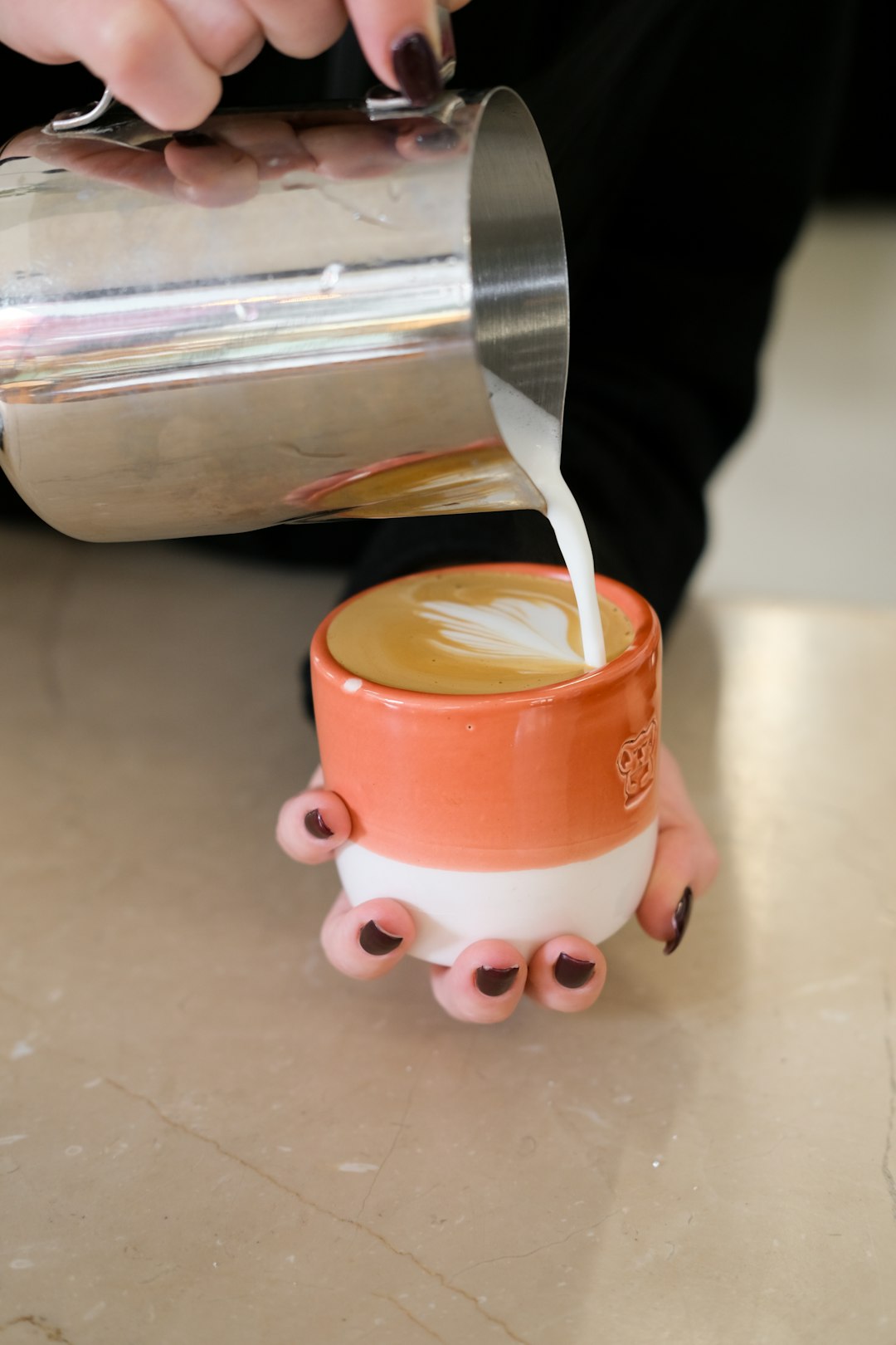 Barista gießt aufgeschäumte Milch in eine Kaffeetasse