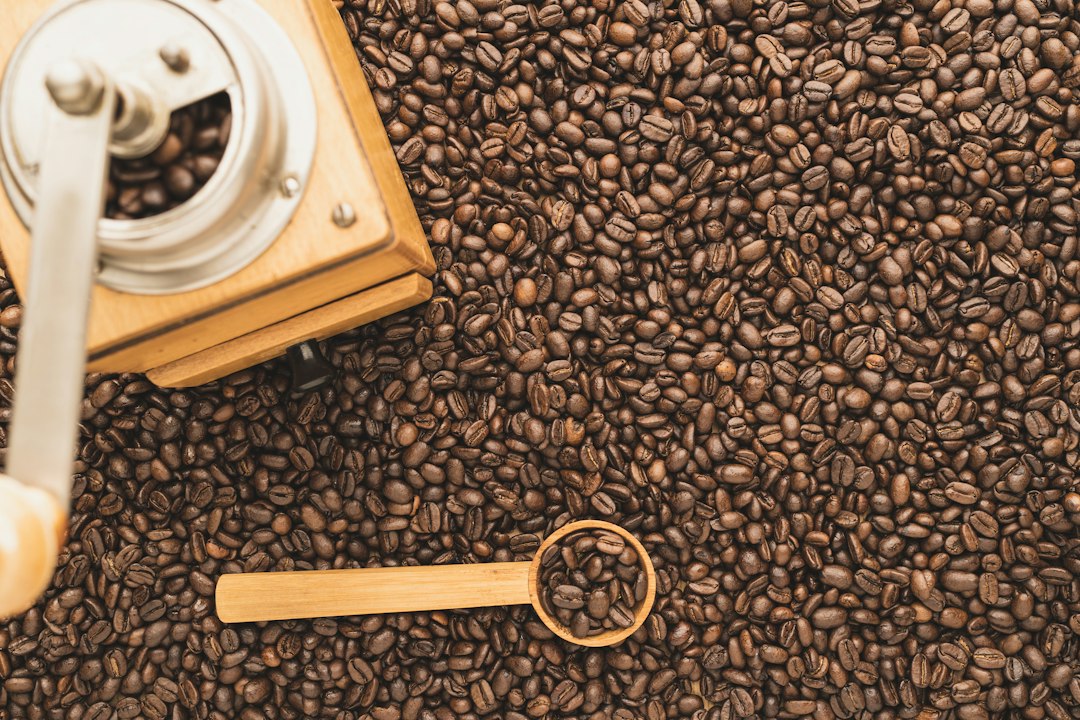 Kaffeemühle neben einem Löffel voller Kaffeebohnen, im Hintergrund weitere Bohnen