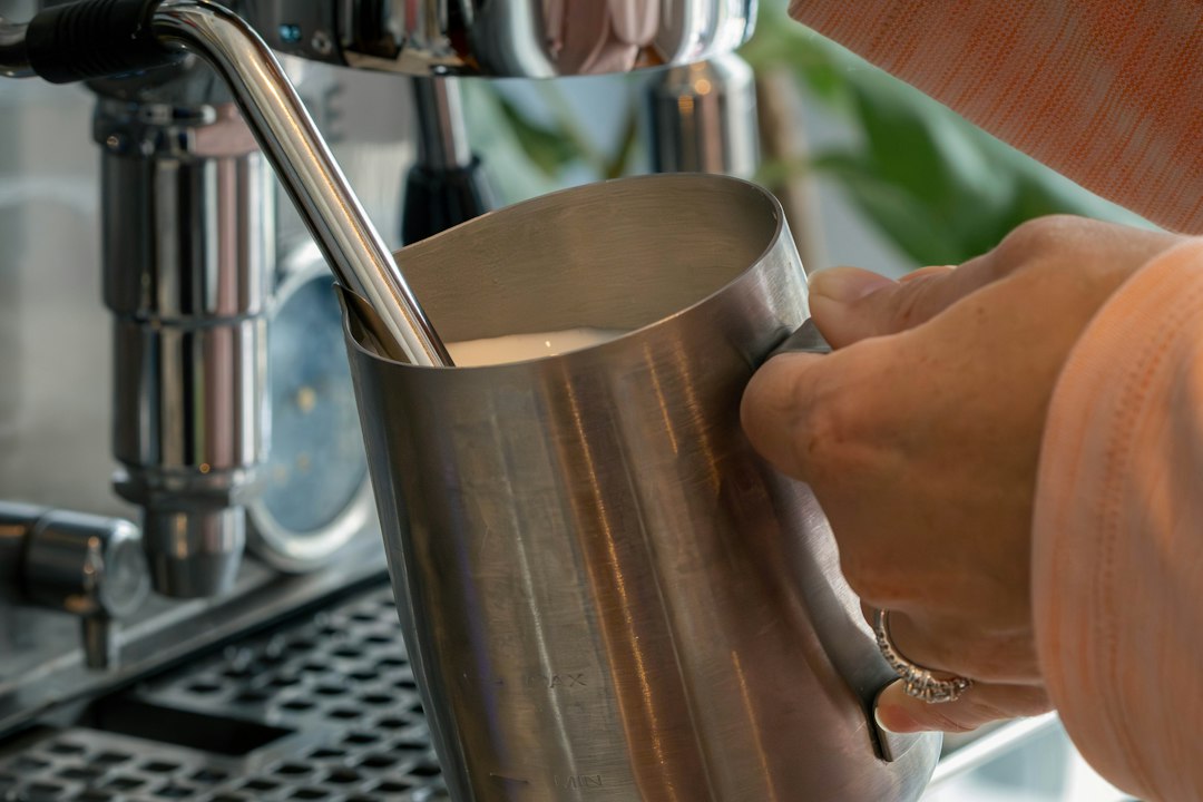Milch wird mit einem Edelstahlkännchen an der Dampflanze einer Siebträgermaschine für zu Hause aufgeschäumt