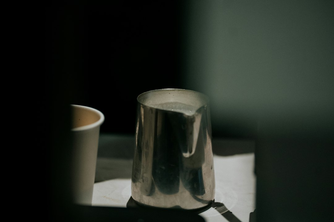 Milchkännchen aus Edelstahl auf einer Theke neben einem Papierbecher