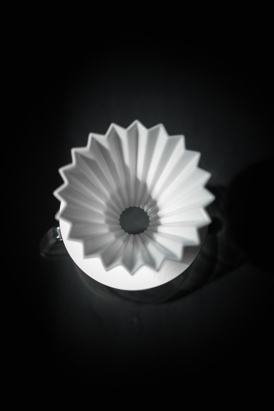 Weißer Origami-Dripper aus Porzellan mit gefalteten Rippen vor dunklem Hintergrund