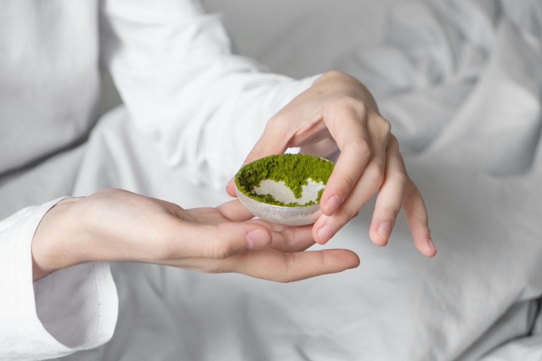 Hand hält ein kleines Schälchen mit grünem Matchapulver