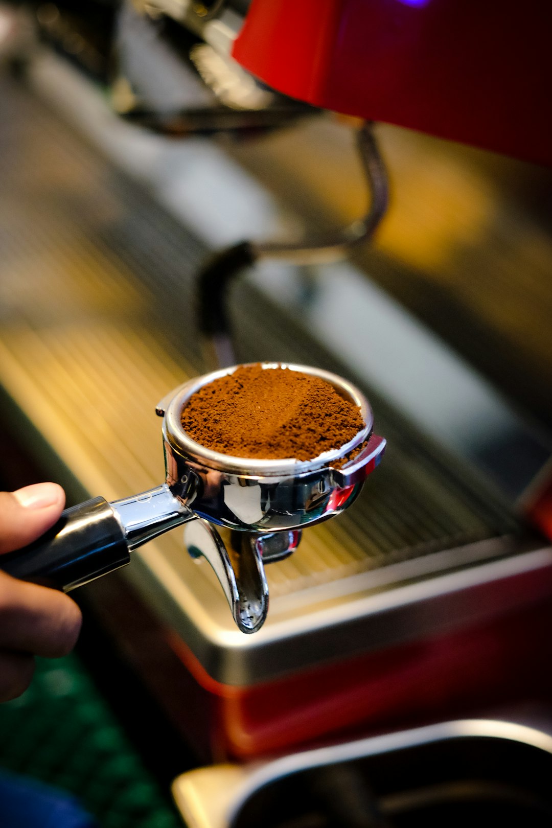 Hand holding a portafilter with ground coffee in front of the espresso machine