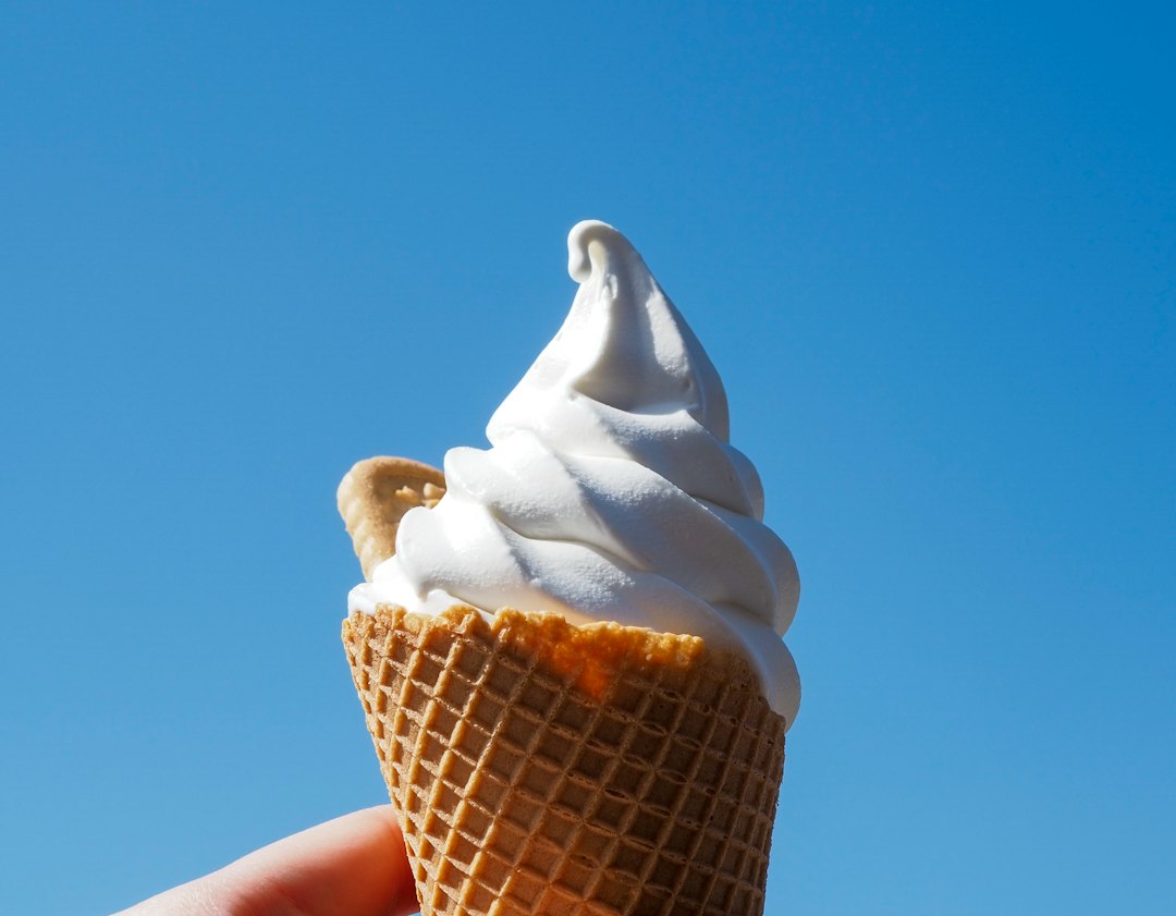 Hand hält Softeis in der Waffel vor blauem Himmel