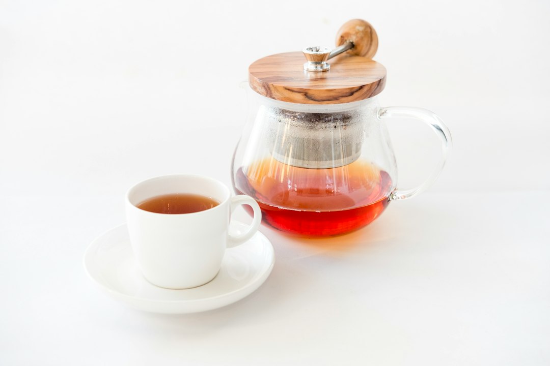 Tee in einer Glaskanne neben einer Teetasse mit Untertasse