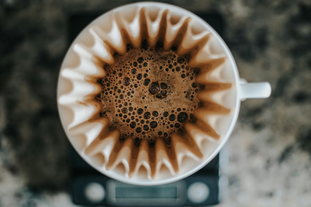Blick von oben in einen weißen Handfilter mit Wellenfilter und aufquellendem Kaffeemehl, darunter eine Waage